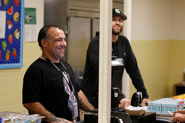 Two men in black shirt smile from behind the cafeteria counter