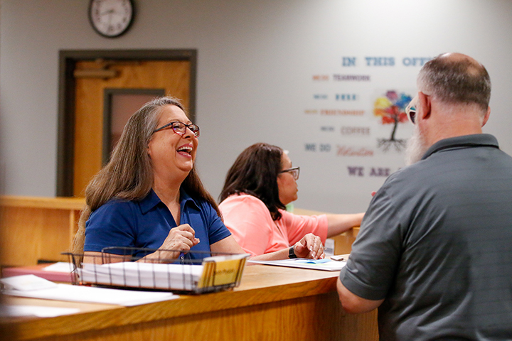 A woman behind the front desk laughs as she talks with a man