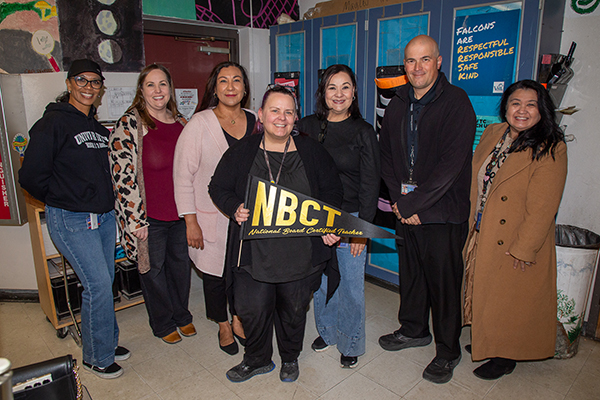 A woman, center, holds an NBCT pennant surrounded by colleagues