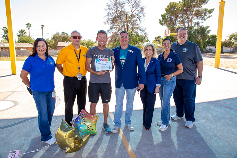 A group of people stand around a man holding an award certificate