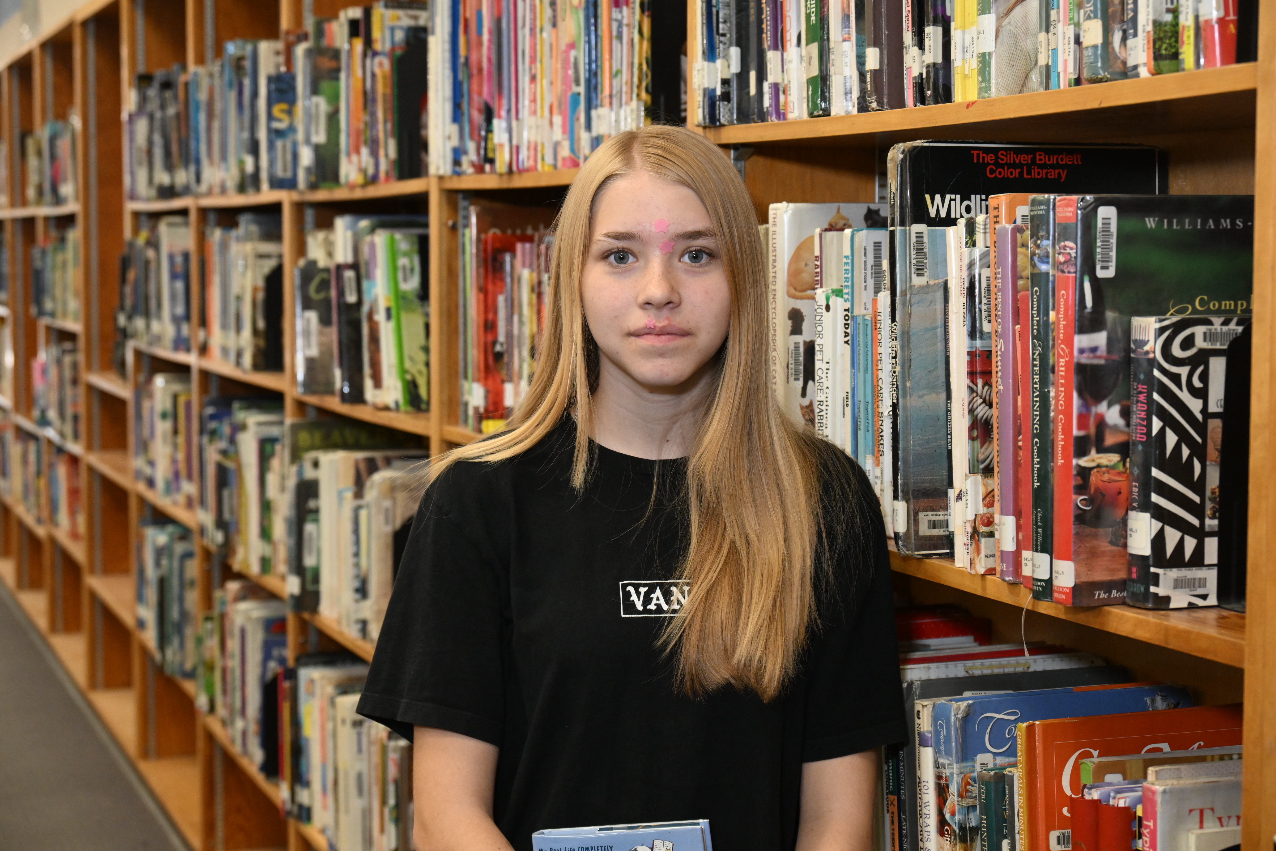 A middle school girl stands in front of bookshelves in the library